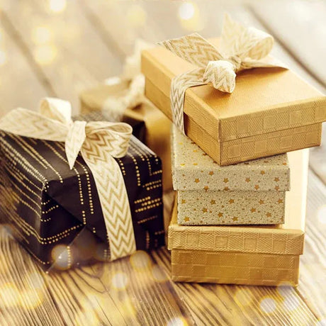 Elegant gift boxes in gold and black with patterned ribbons on a rustic wooden surface with warm bokeh lights.