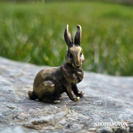 Small antique-style bronze rabbit figurine sitting on a textured grey stone against a blurred green garden background.